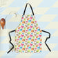 The Pugalicious Apron by My Favourite Colour is Rainbow boasts black straps and a vibrant pattern with orange, yellow, blue and pink pugs. In the background are essential kitchen items like a wooden spoon and spatula.