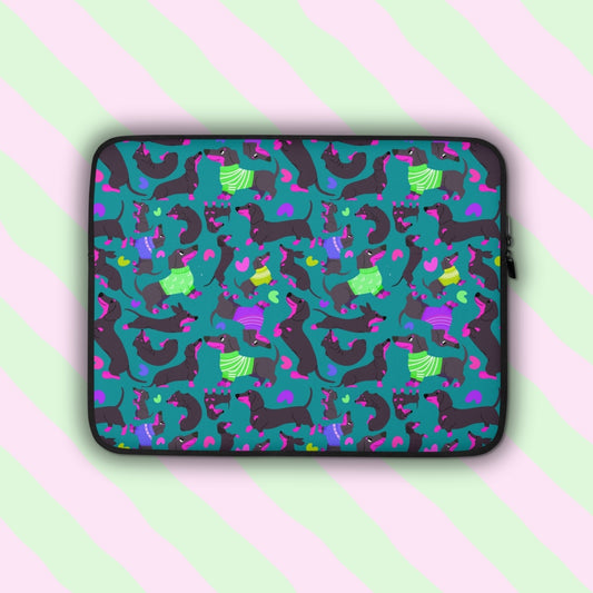 The Silly Sausages Laptop Sleeve – Green by My Favourite Colour is Rainbow features playful dachshunds in green and purple on a dark green backdrop with matching coloured hearts. It has a double black zipper and padded zipper binding.  It is shown on a pastel background.  The print is on only one side of the laptop sleeve, the other side is black.