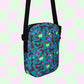 The Silly Sausages Mini Crossbody Bag by My Favourite Colour is Rainbow features a vibrant dolphin and wave pattern in purple, green, and blue. It has an adjustable strap for comfort and pops against a pink and light green checkered background.