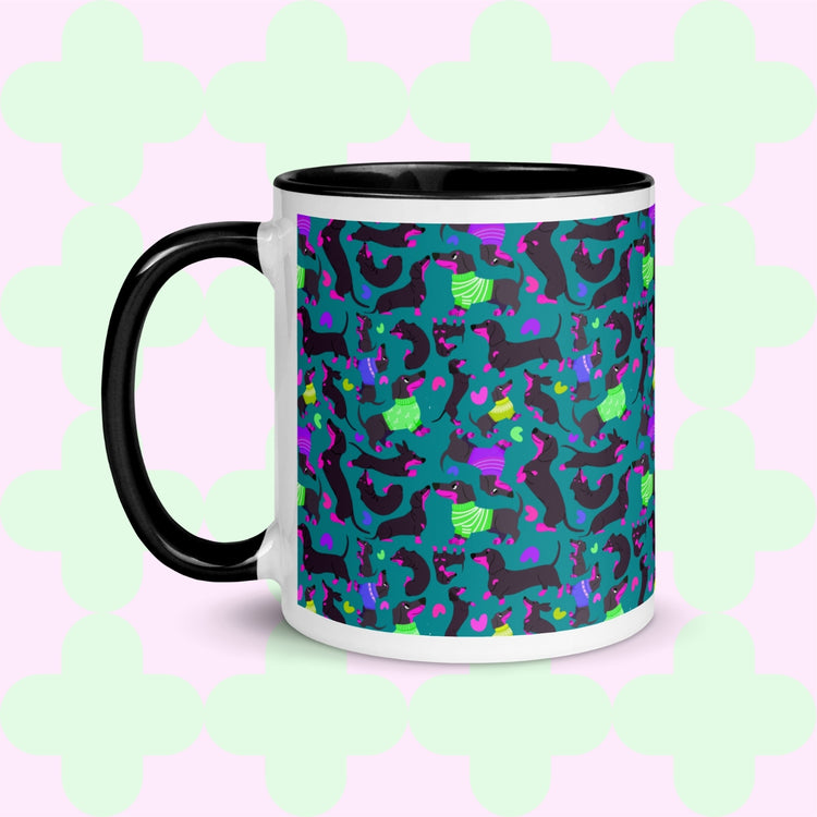 The Silly Sausages Mug by My Favourite Colour is Rainbow features playful black-and-pink dachshunds wearing in green and purple jumpers on a dark teal background.  The mug has a black handle and interior.