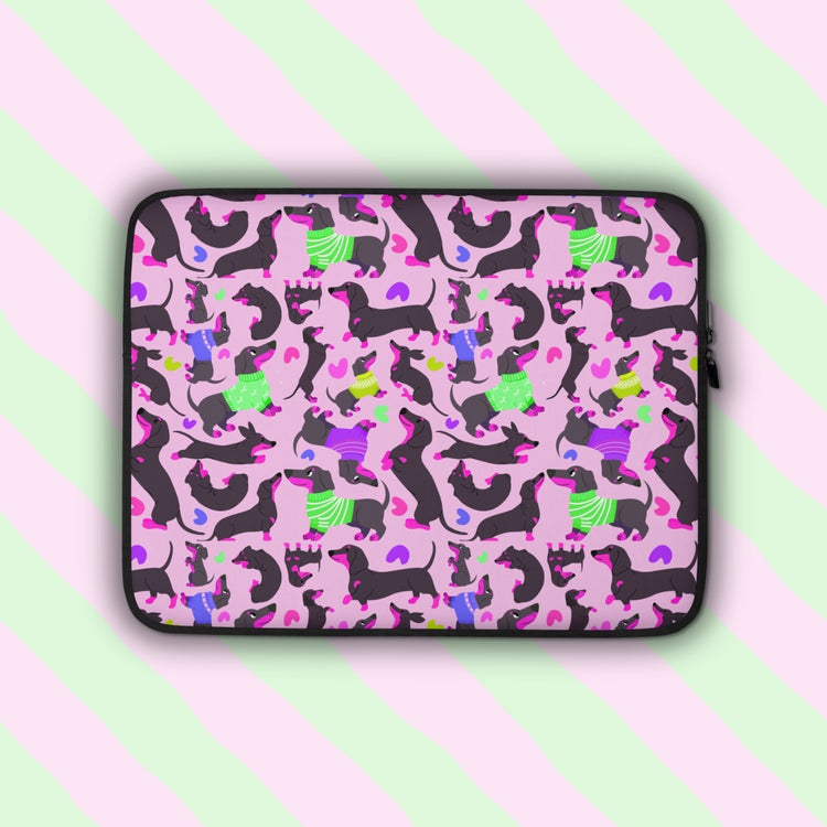 The Silly Sausages Laptop Sleeve – Pink by My Favourite Colour is Rainbow features playful dachshunds in green and purple sweaters on a light pink backdrop with matching coloured hearts. Shown on a pastel background.