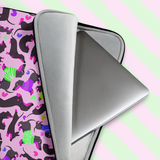 A laptop is snugly nestled in the Silly Sausages Laptop Sleeve – Pink by My Favourite Colour is Rainbow, featuring dachshunds in colorful sweaters on a pink heart backdrop. 