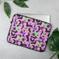 A laptop peeks out from the 15 inch Silly Sausages Laptop Sleeve – Pink by My Favourite Colour is Rainbow, showcasing a fun dachshund pattern. This scratch-proof, splash-resistant sleeve sits on a gray surface surrounded by green leaves.