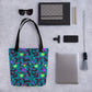 Flat lay featuring the Silly Sausages tote bag by My Favourite Colour is Rainbow, with a fun pattern of black-and-pink dachshunds wearing green and purple jumpers on a dark teal background.  Surrounding it are sunglasses, a mobile phone, laptop, notebooks and pens.