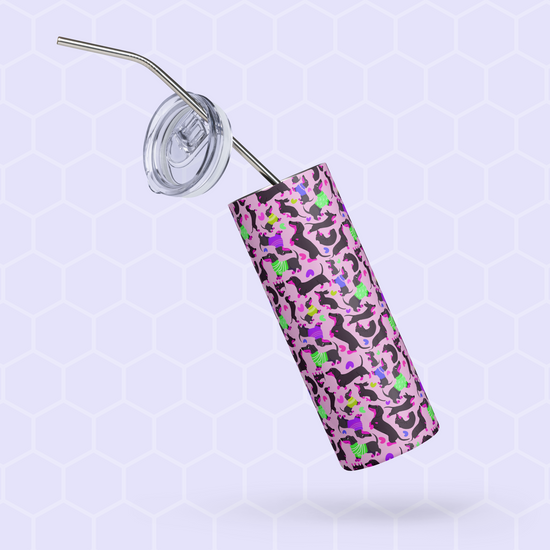 The Silly Sausages Stainless Steel Tumbler by My Favourite Colour is Rainbow, featuring a pink, black, green, and purple abstract pattern with a metal straw and lid, is tilted against a light blue hexagonal patterned background.