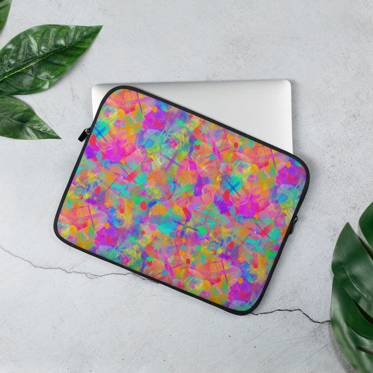 The 15 inch Splotches and Crosses Laptop Sleeve by My Favourite Colour is Rainbow features a vibrant design of splashes of colour and contrasting large cross shapes in pink, blue, yellow, orange and green. Its displayed on a light gray surface with green leaves arranged around it.