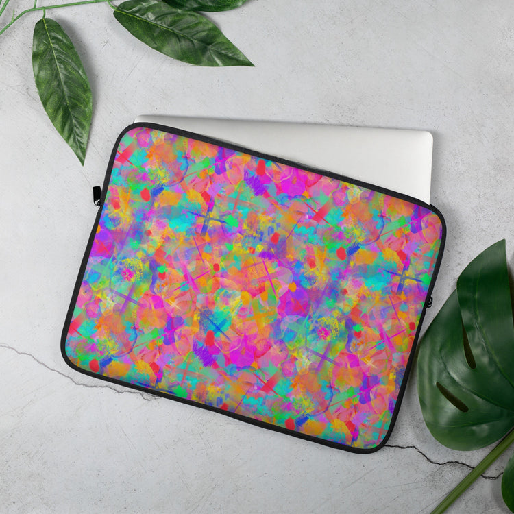 The Splotches and Crosses Laptop Sleeve by My Favourite Colour is Rainbow features vibrant pink, green, blue, and orange hues on a concrete backdrop. With partially visible leaves surrounding it, the abstract design makes a bold tech statement.