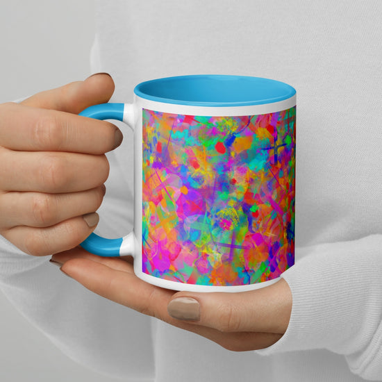 A person wearing a white top and painted nails holds the Splotches and Crosses Mug by My Favourite Colour is Rainbow. The mug features a colorful abstract design with blue, pink, orange, and green splashes and has a blue interior.