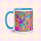 The Splotches and Crosses Mug by My Favourite Colour is Rainbow is a white mug with a light blue interior and handle, featuring a vibrant abstract design with splashes of green, blue, pink, and orange. 