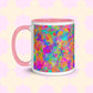 The Splotches and Crosses Mug by My Favourite Colour is Rainbow is a white mug with a pink interior and handle, featuring a vibrant abstract design with splashes of green, blue, pink, and orange. 