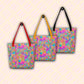 Three Splotches and Crosses Tote Bags by My Favourite Colour is Rainbow hanging on hooks, showing red, yellow and black handles.  The bags feature an abstract pattern of pink, blue, green, and orange splashes.