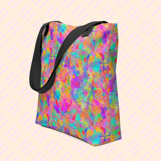 The Splotches and Crosses Tote Bag by My Favourite Colour is Rainbow features an abstract pattern of pink, blue, green, and orange splashes.  This version has black straps.