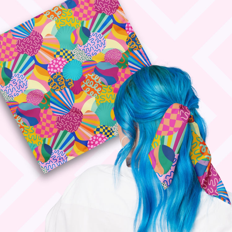 Two views of the 'Squiggs and Stripes' Bandana by My Favourite Colour is Rainbow.  At top left, a flat lay of the bandana.  At bottom right, a person with vibrant blue hair is seen from behind, wearing the bandana in her hair.  The bandana features a colourful abstract design with circles, waves, stripes, and checkered patterns in pink, blue, green, yellow, and orange. 