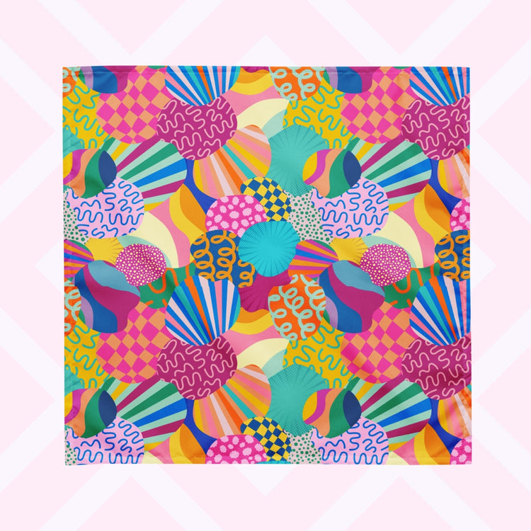 The Squiggs and Stripes Bandana by My Favourite Colour is Rainbow features a colourful abstract design with circles, waves, stripes, and checkered patterns in pink, blue, green, yellow, and orange. 