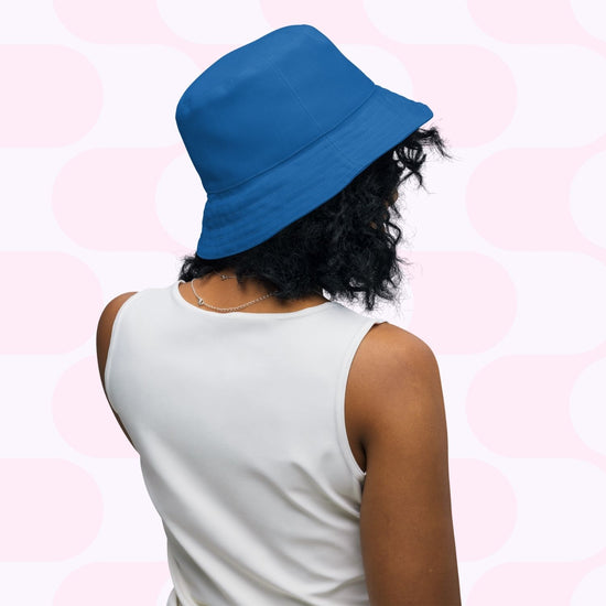 A person wearing a Squiggs and Stripes Reversible Bucket Hat by My Favourite Colour is Rainbow and a sleeveless white top, facing away. The backdrop showcases a light pink and white abstract pattern, adding Style BFF flair.