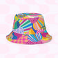 The Squiggs and Stripes Reversible Bucket Hat by My Favourite Colour is Rainbow showcases an abstract mix of shapes, lines, and geometric designs in vibrant pink, blue, yellow, and green on a white background with light pink circles. Available in multiple sizes for the perfect fit.