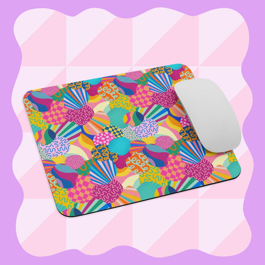 A white computer mouse sits on the Squiggs and Stripes Mouse Pad by My Favourite Colour is Rainbow, showcasing a vibrant abstract pattern of various shapes and bright colors against a pink and white checkered background with wavy lavender borders.