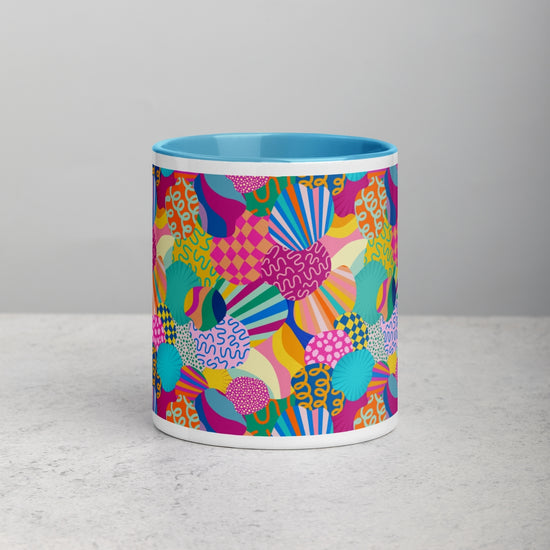 The Squiggs and Stripes Mug by My Favourite Colour is Rainbow has a bright blue interior and sits on a light gray surface, with an exterior featuring multicoloured abstract shapes like swirls, circles, and geometric patterns.