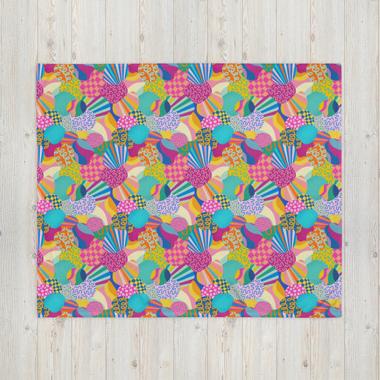 The My Favourite Colour is Rainbow Squiggs and Stripes Throw Blanket showcases a vibrant design with colorful, abstract geometric shapes and stripes in pink, blue, yellow, and green on a flat square surface against a light wooden background with visible grain.