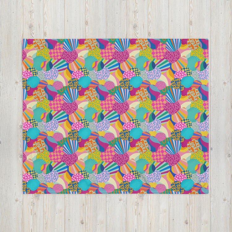 The My Favourite Colour is Rainbow Squiggs and Stripes Throw Blanket showcases a vibrant design with colorful, abstract geometric shapes and stripes in pink, blue, yellow, and green on a flat square surface against a light wooden background with visible grain.