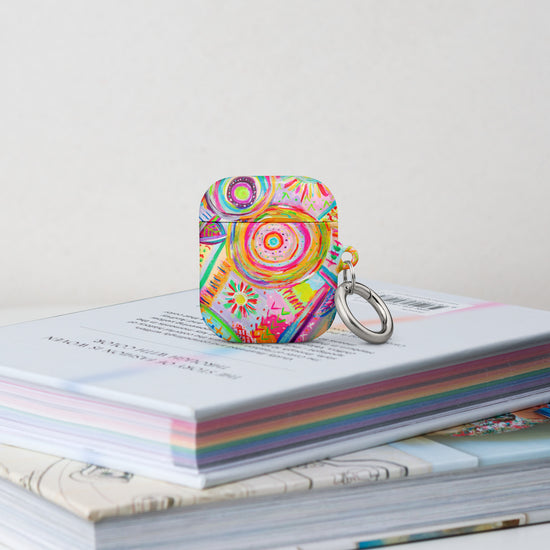 The Summer Sorbet Airpods Gen 2 Case stands on a stack of books.  It features a colourful abstract design with swirls, flowers, and geometric shapes in bright hues. 
