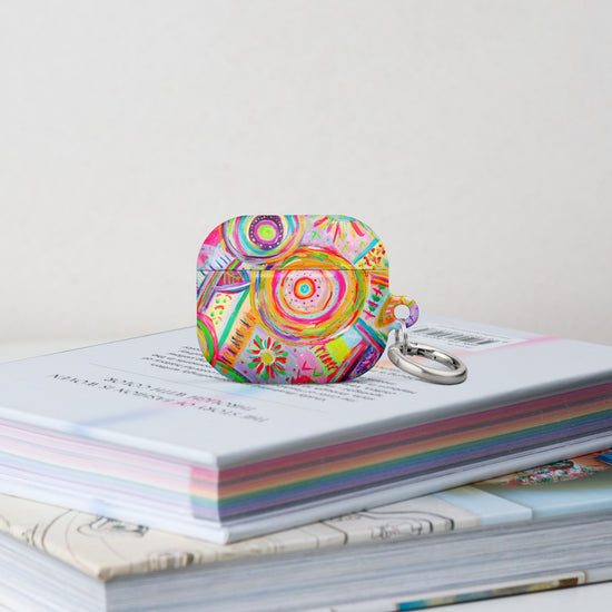 The Summer Sorbet Airpods Gen 3 Case stands on a stack of books.  It features a colourful abstract design with swirls, flowers, and geometric shapes in bright hues. 
