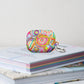 The Summer Sorbet Airpods Pro Gen 1  Case stands on a stack of books.  It features a colourful abstract design with swirls, flowers, and geometric shapes in bright hues. 
