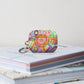 The Summer Sorbet Airpods Pro Gen 2  Case stands on a stack of books.  It features a colourful abstract design with swirls, flowers, and geometric shapes in bright hues. 
