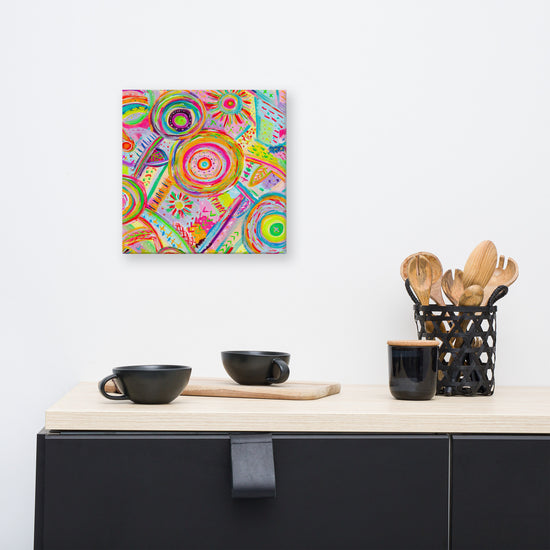 A minimalist kitchen showcases two black cups on a light wooden tray on a black countertop. The Summer Sorbet Canvas Artwork by My Favourite Colour is Rainbow adds vibrancy to the white wall above. To the right, a black basket with wooden utensils completes the stylish ensemble.