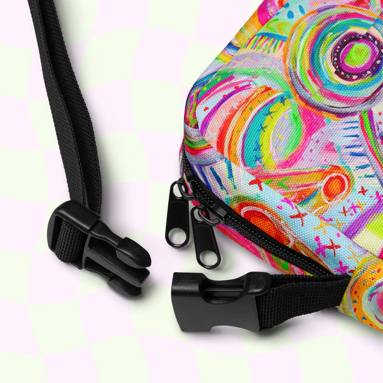 Close-up of the My Favourite Colour is Rainbow Summer Sorbet Mini Crossbody Bag, showcasing its vibrant circles and swirls design, two black zippers, and adjustable straps on a light checkered background.