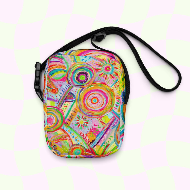 The Summer Sorbet Mini Crossbody Bag by My Favourite Colour is Rainbow features a colorful, abstract pattern with circles and spirals in vivid pink, green, yellow, and blue set against a soft pale pink and green checkered background. It includes adjustable straps for convenience.