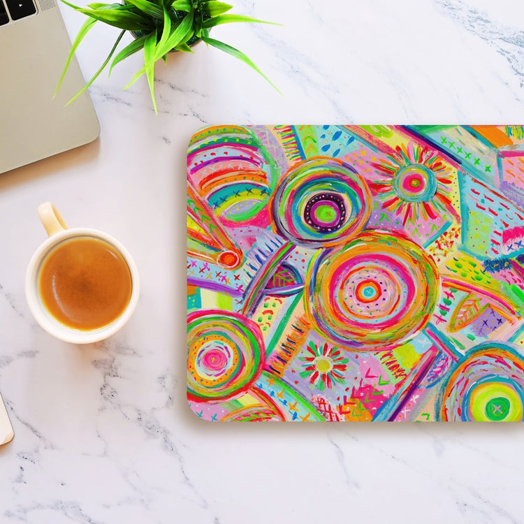 The Summer Sorbet Mouse Pad by My Favourite Colour is Rainbow, featuring abstract pink, yellow, and green circular patterns, sits on a marble desk near a coffee cup and laptop corner. A small green plant complements the setup with a touch of nature.