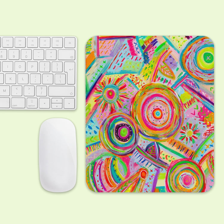 The Summer Sorbet Mouse Pad by My Favourite Colour is Rainbow displays a vibrant abstract pattern with bright circles and lines, placed beside a white keyboard and mouse on a light green surface.