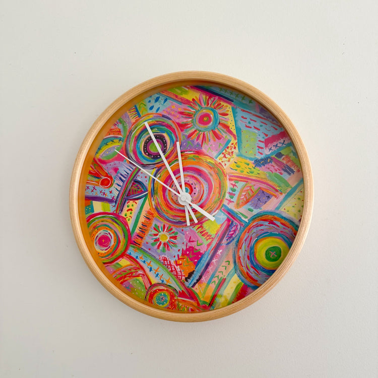 The Summer Sorbet Wall Clock by My Favourite Colour is Rainbow has a silent mechanism and wooden frame surrounding vibrant abstract designs. Bold pink, green, blue, yellow, and orange swirls are set against white hands pointing to 10:09.