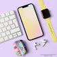 A keyboard, a pastel gradient screen smartphone, and wireless earbuds in a The Rainbow Connection AirPods Case are arranged with a yellow-banded smartwatch on a light purple surface.