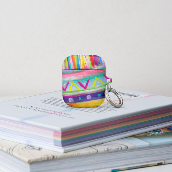 The Rainbow Connection Airpods Gen 1 Case stands on a stack of books.  It features  an abstract design of colourful green, pink, yellow, blue, and purple stripes, dots, and zigzags.