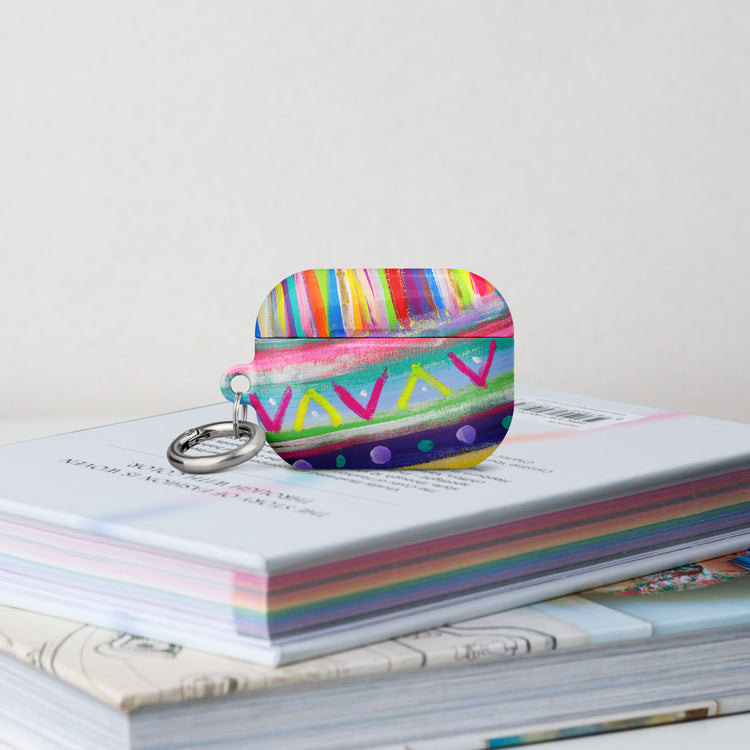 The Rainbow Connection Airpods Pro Gen 2  Case stands on a stack of books.  It features  an abstract design of colourful green, pink, yellow, blue, and purple stripes, dots, and zigzags. 
