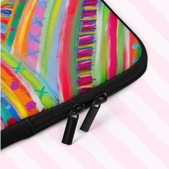 A closeup of The Rainbow Connection Laptop Sleeve by My Favourite Colour is Rainbow.  The sleeve features a colourful abstract design of curved lines, dots, and triangles in vibrant pink, orange, green, blue, and yellow.  It includes a black padded binding with dual zipper pull tabs for added convenience.  The print is on only one side of the laptop sleeve, the other side is black.   It is shown on a pastel background.
