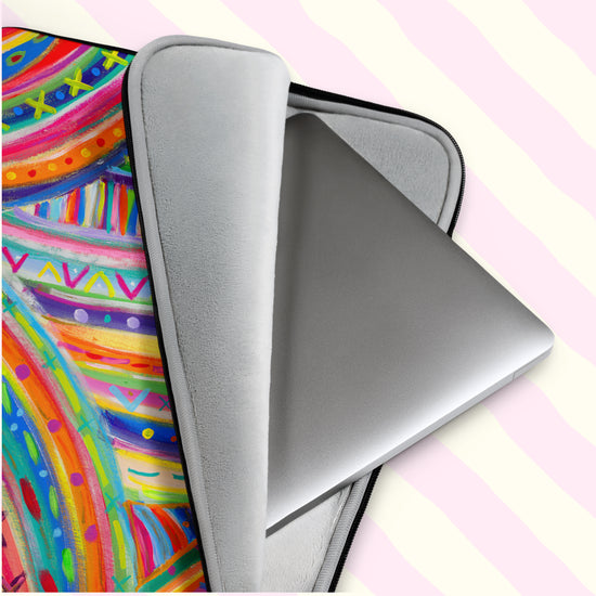 A silver laptop peeks out of The Rainbow Connection Laptop Sleeve by My Favourite Colour is Rainbow. This scratch-proof sleeve features a colourful abstract design of curved lines, dots, and triangles in vibrant pink, orange, green, blue, and yellow.  It has a grey padded interior to keep your laptop safe from scratches.  The print is on only one side of the laptop sleeve, the other side is black. It is shown on a pastel background.