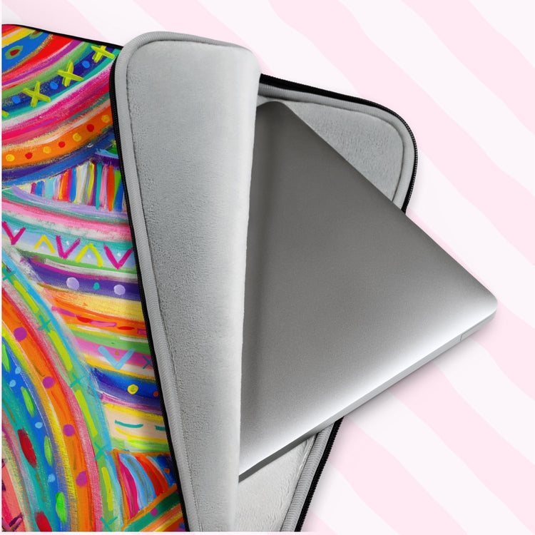 A silver laptop peeks out of The Rainbow Connection Laptop Sleeve by My Favourite Colour is Rainbow. This scratch-proof sleeve features a colourful abstract design of curved lines, dots, and triangles in vibrant pink, orange, green, blue, and yellow.  It has a grey padded interior to keep your laptop safe from scratches.  The print is on only one side of the laptop sleeve, the other side is black. It is shown on a pastel background.