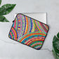 The 13 inch 'The Rainbow Connection' Laptop Sleeve by My Favourite Colour is Rainbow, featuring a colourful abstract design of curved lines, dots, and triangles in vibrant colours, partially covers a silver laptop.  It is shown on a light grey surface with green leaves on both sides.