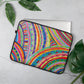 The 15 inch 'The Rainbow Connection' Laptop Sleeve by My Favourite Colour is Rainbow, featuring a colourful abstract design of curved lines, dots, and triangles in vibrant colours, partially covers a silver laptop.  It is shown on a light grey surface with green leaves on both sides.