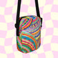 The Rainbow Connection Mini Crossbody Bag by My Favourite Colour is Rainbow features a vibrant psychedelic pattern with swirls and dots in pink, orange, green, and blue. Its displayed on a pink and cream checkerboard background with black adjustable straps and side accents.