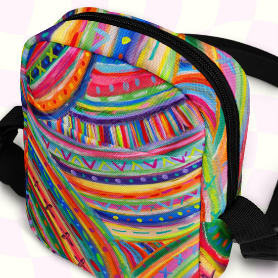 The Rainbow Connection Mini Crossbody Bag by My Favourite Colour is Rainbow features a vibrant abstract design with swirling patterns in rainbow hues, a black zipper, adjustable straps, and roomy pockets against a subtle light background.