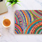 A vibrant mouse pad, The Rainbow Connection by My Favourite Colour is Rainbow, featuring abstract curved patterns on a marble surface. Nearby are a cup of coffee and a laptop, with a small green plant adding nature to the scene.