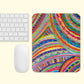 A white keyboard and mouse on a light pink surface beside The Rainbow Connection Mouse Pad by My Favourite Colour is Rainbow, showcasing vibrant abstract patterns in blue, green, red, yellow, and pink.