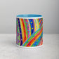 Front view of the Rainbow Connection Mug by My Favourite Colour is Rainbow, featuring a vibrant abstract design with bright blue, pink, orange, and green stripes, dots, and triangles. It has a light blue interior and rests on a grey surface.