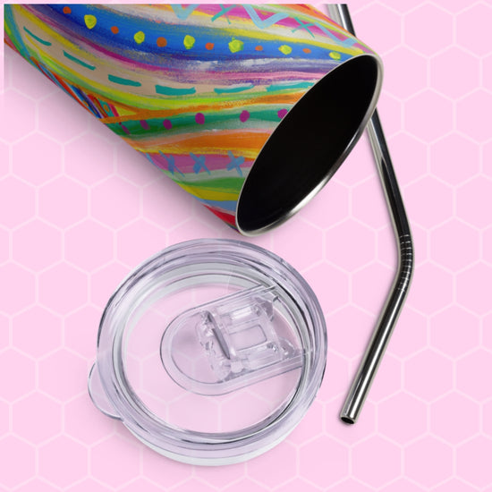 The Rainbow Connection Stainless Steel Tumbler by My Favourite Colour is Rainbow showcases vibrant abstract patterns on a pink hexagonal background. It features an open top with a clear lid, accompanied by a metal straw placed next to it.