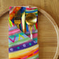 The Rainbow Connection Cloth Napkin Set of 4 by My Favourite Colour is Rainbow features a gold fork, knife, and spoon tucked into a vibrant napkin with rainbow stripes. Arranged on a round wooden plate against a warm wooden table, this setting offers an elegant dining upgrade.