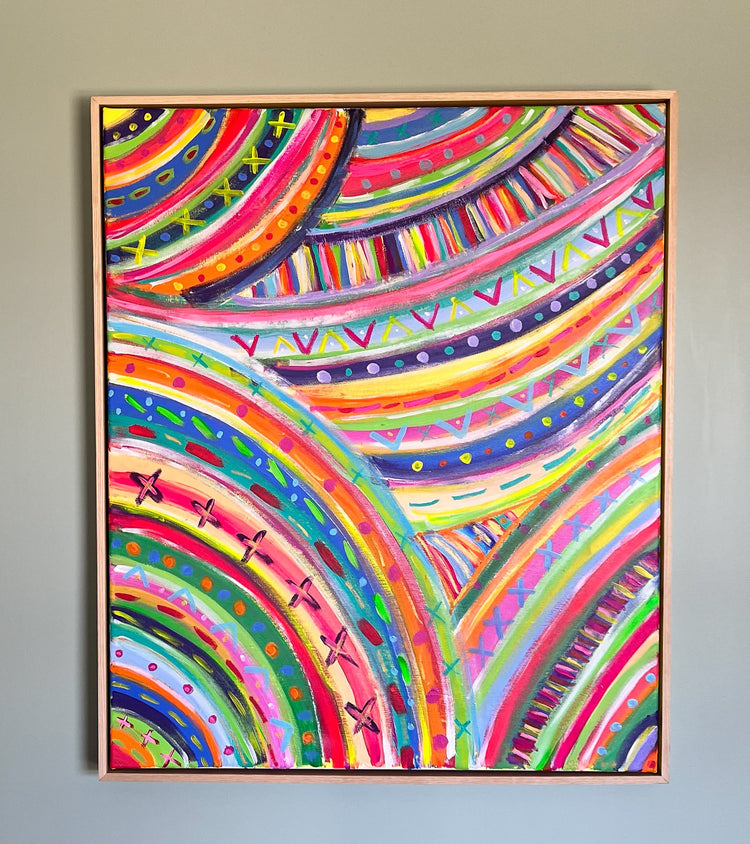 Acrylic on canvas, The Rainbow Connection Framed Original Painting by My Store features swirling arcs with vibrant patterns of stripes, dots, and crosses. Its professionally framed in light wood, creating a standout display against a gray wall.